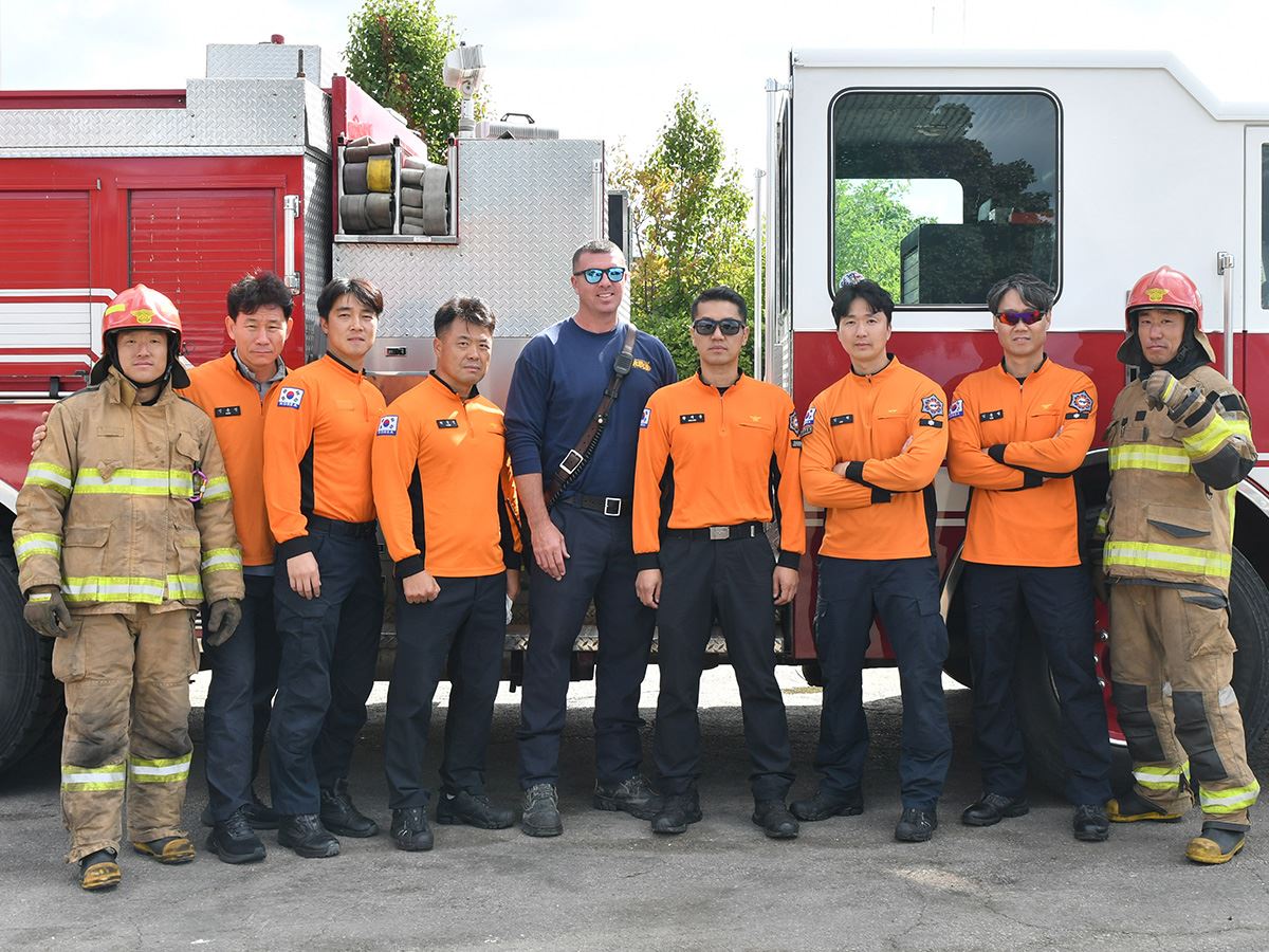Members of Korean Disaster Relief Team pose with Fire Academy instructor by fire truck. 